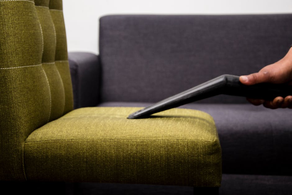 A mustard yellow armchair with a plush, tufted backrest and wide armrests, placed on a smooth, light grey concrete floor against a plain white wall. The armchair features caster wheels underneath, all